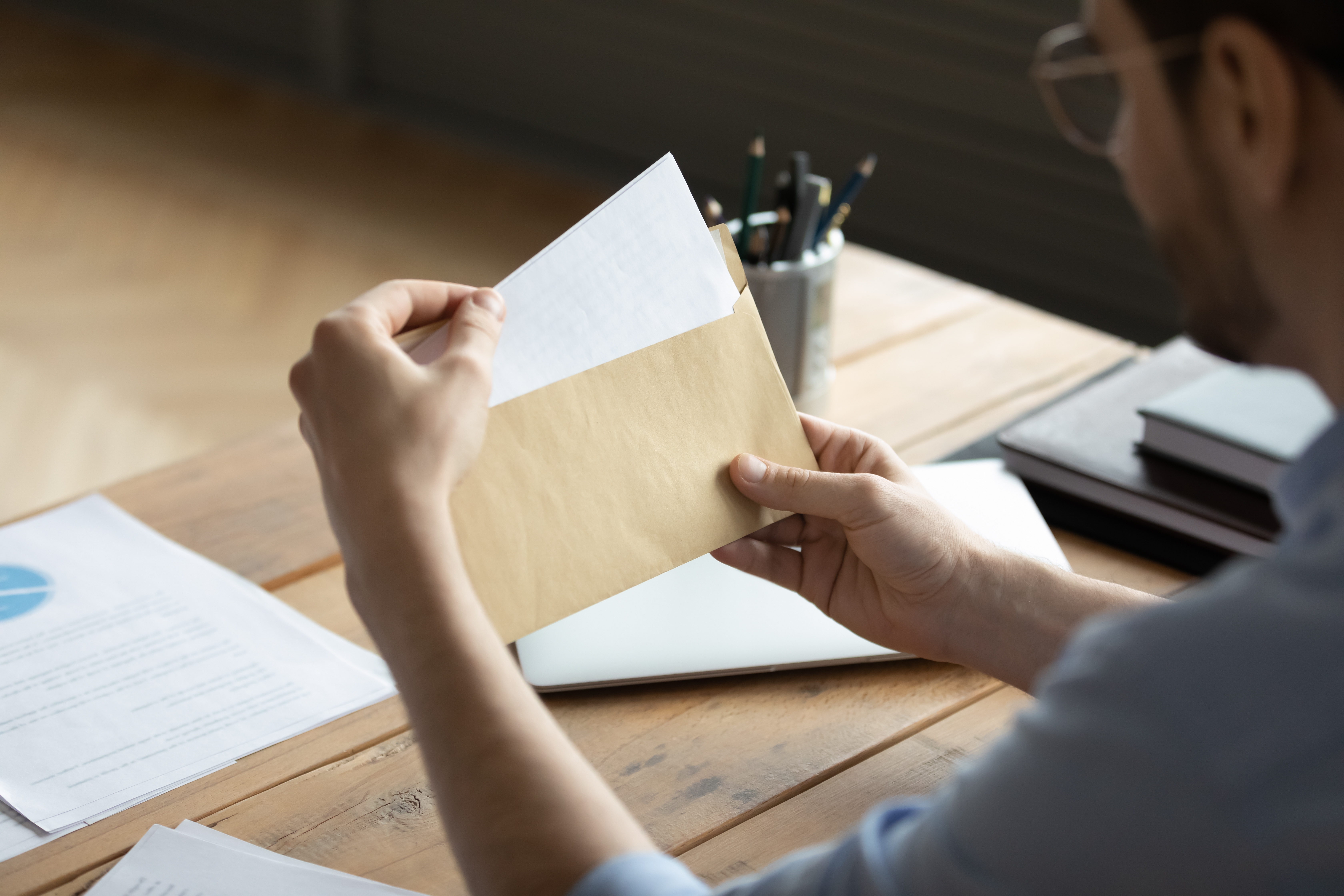 Business owner holding an envelope with an official letter at an office desk, representing receipt of a legal or government notice