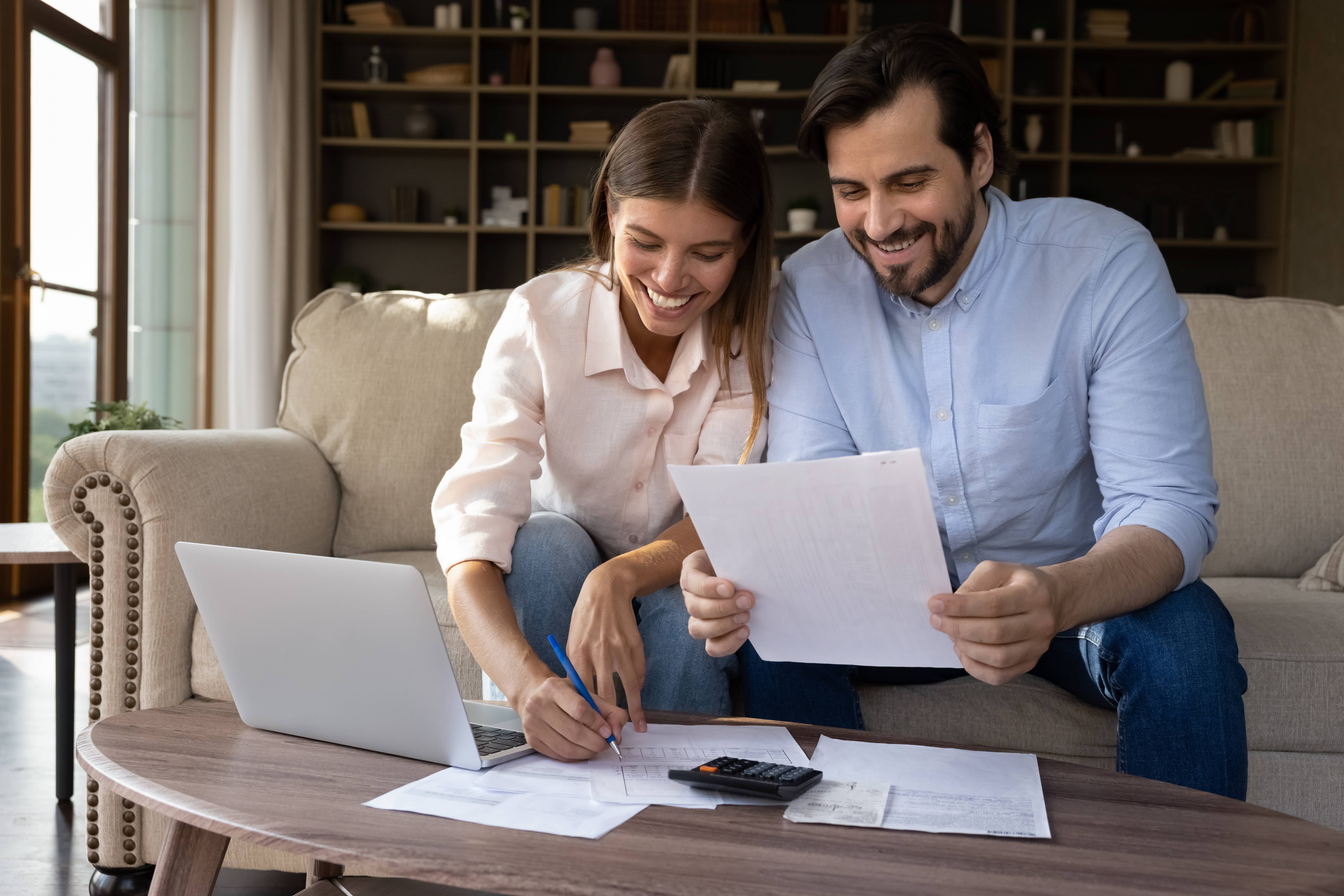Smiling young couple sitting at home reviewing household mail and organizing documents together