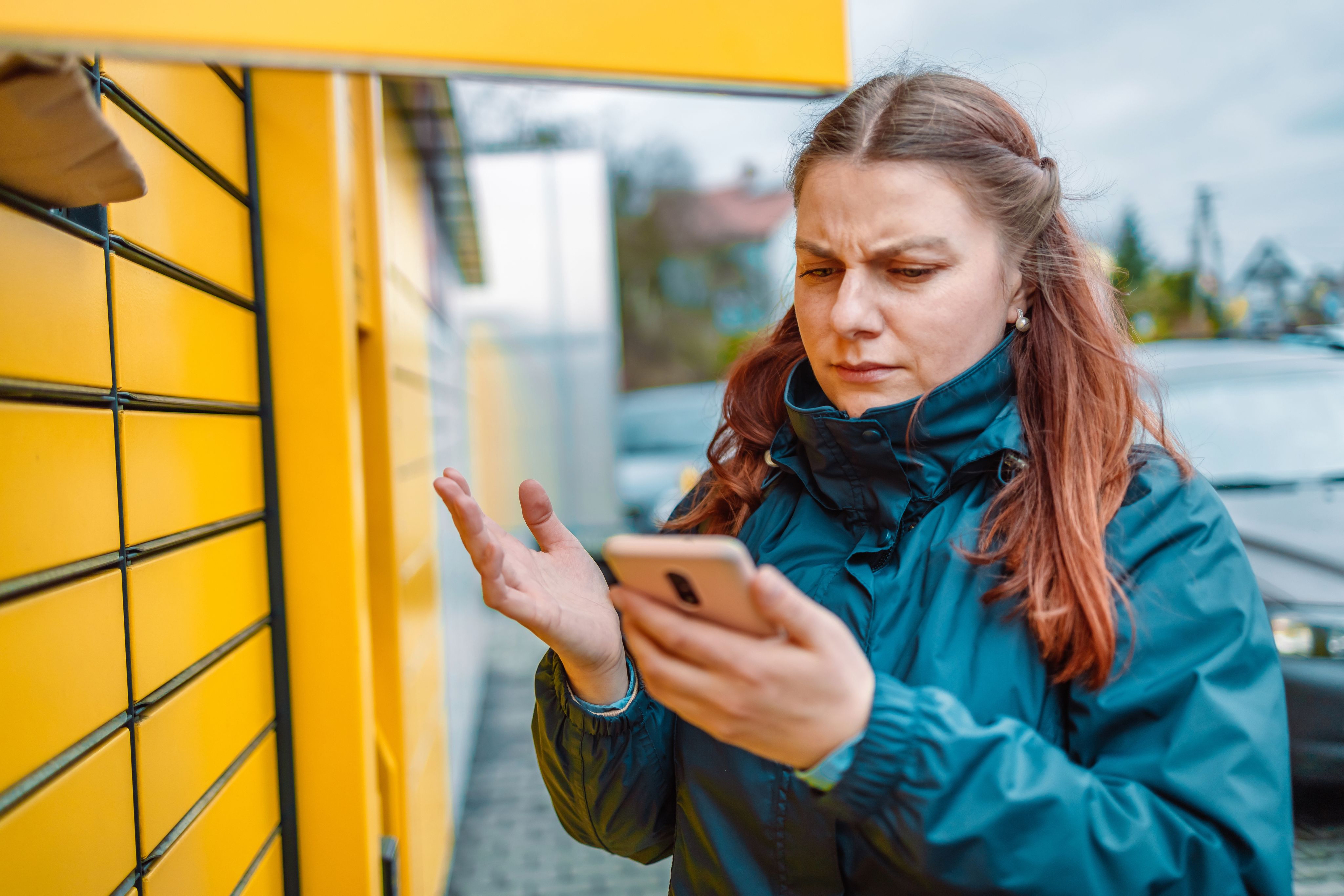 Personal package locker Frustrated woman looking at smartphone in front of yellow package lockers