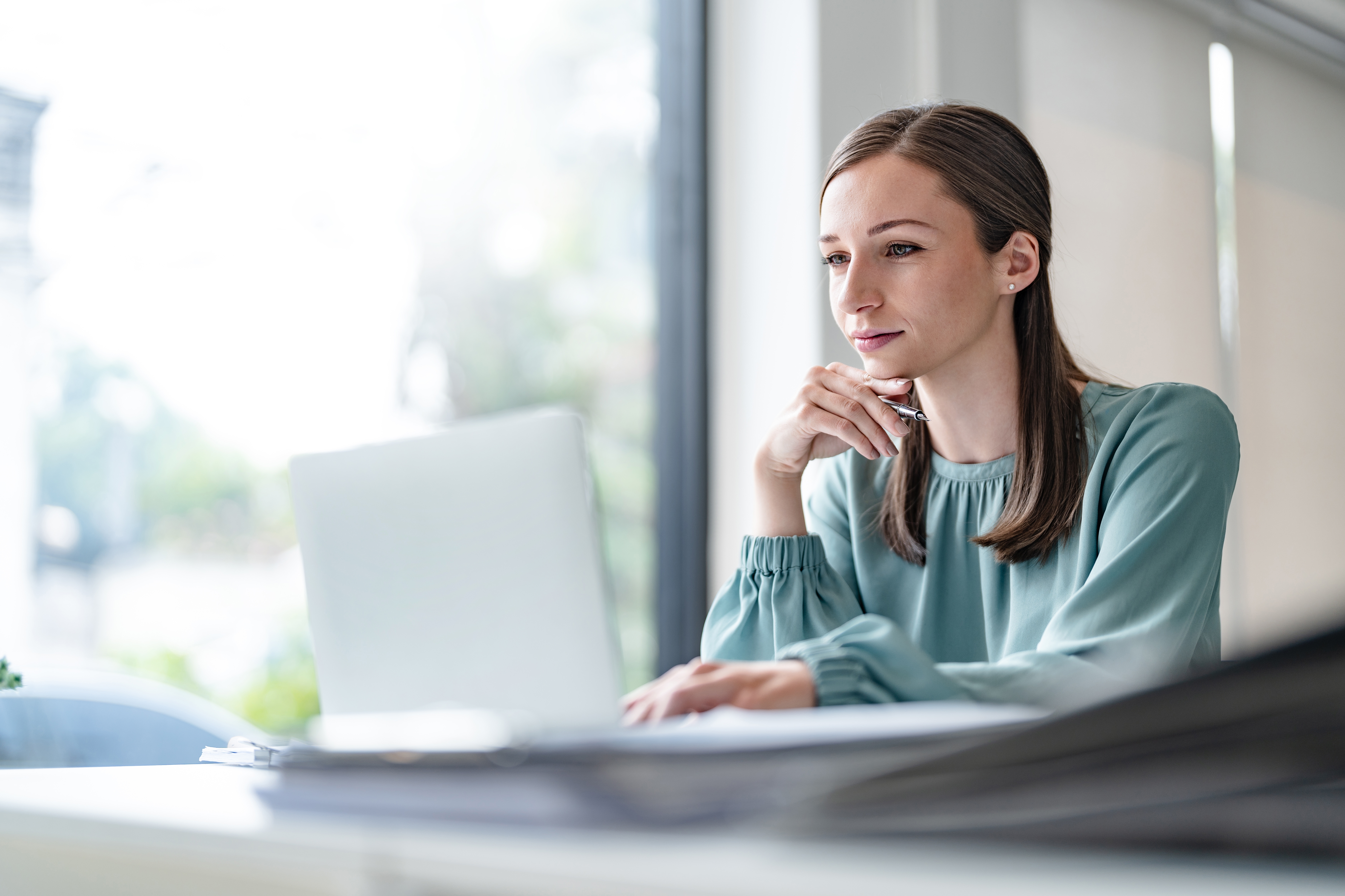 Woman in a blouse sitting at a laptop looking curiously at the screen